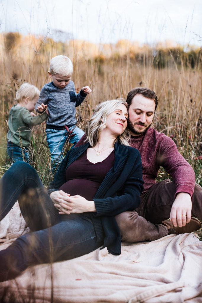 pregnant mom with husband in field with two older boys by charlottesville maternity photographer