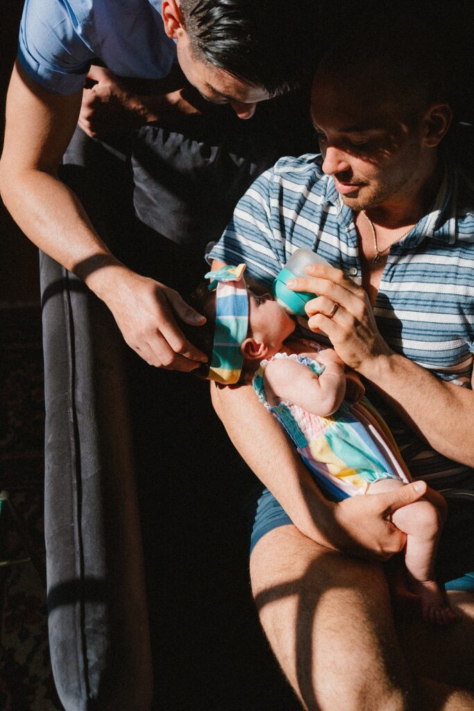 natural newborn photos at home with two dads bottle feeding baby girl