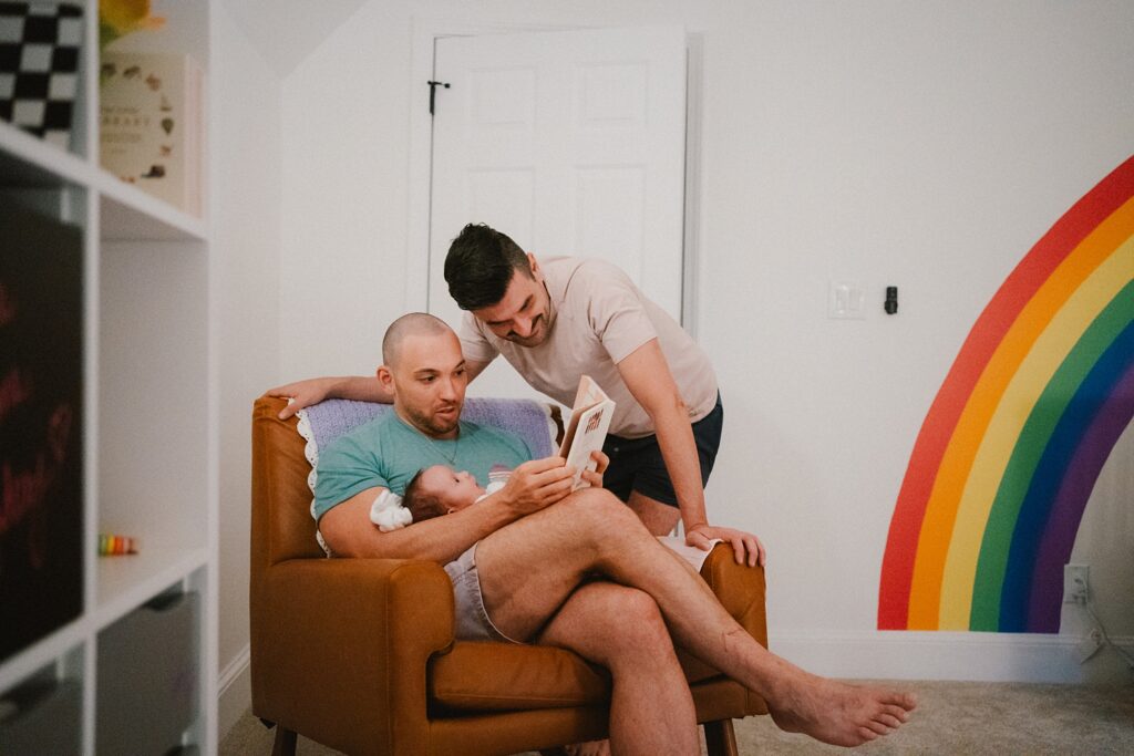 two dads reading books to newborn daughter 