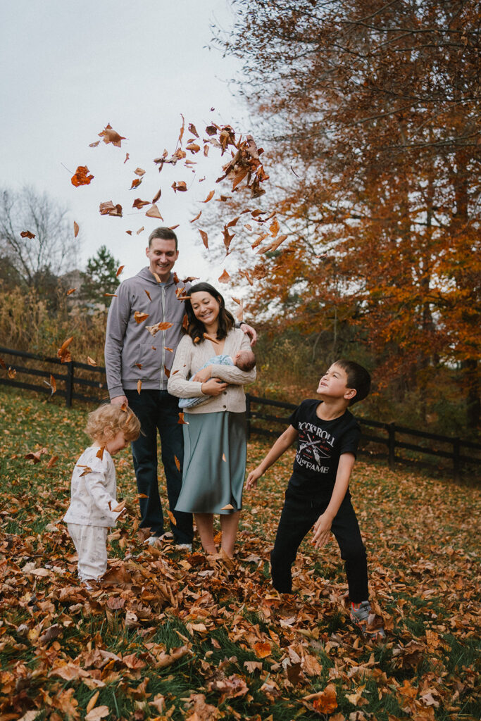 family with newborn tossing leaves in the backyard